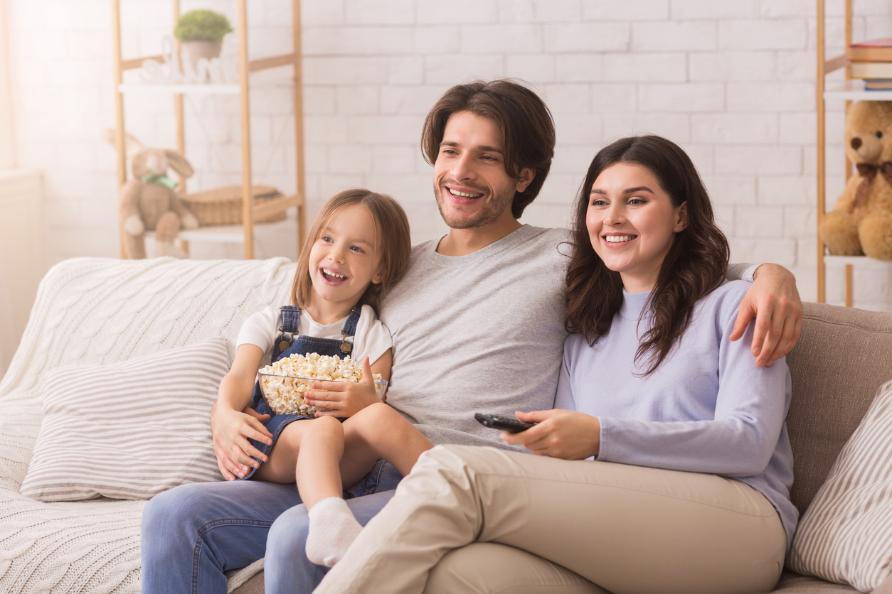 Family Of Three Relaxing At Home, Watching TV And Eating Popcorn