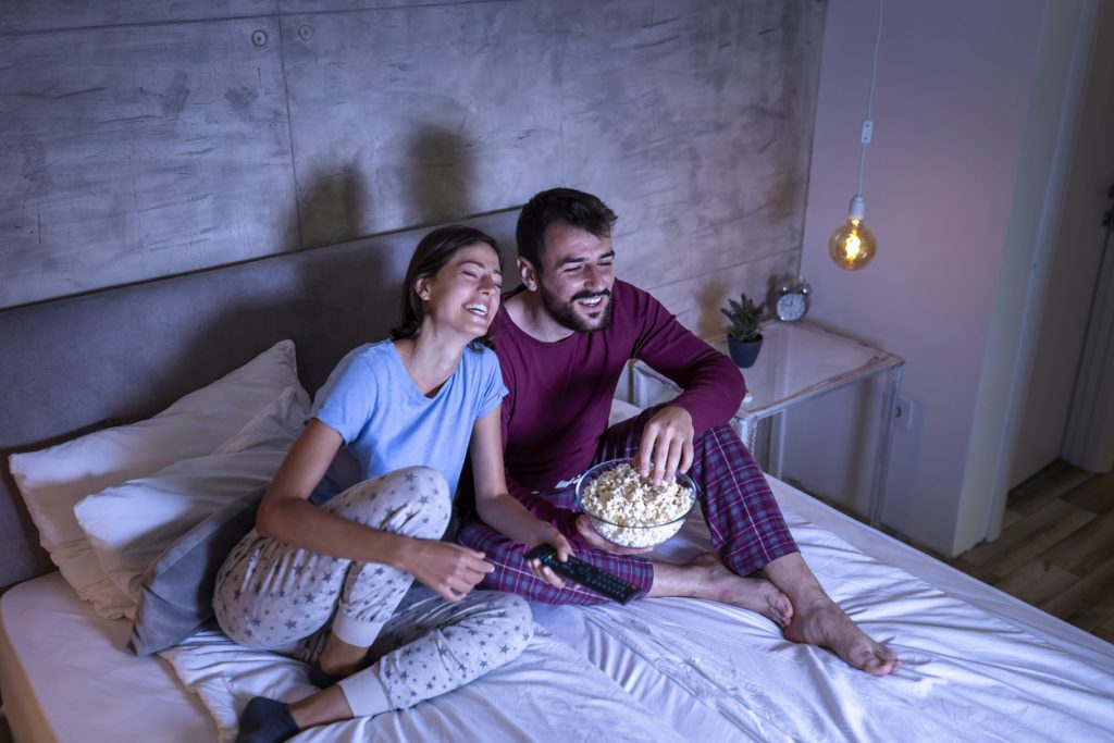 A couple laughing and smiling watching TV in bed