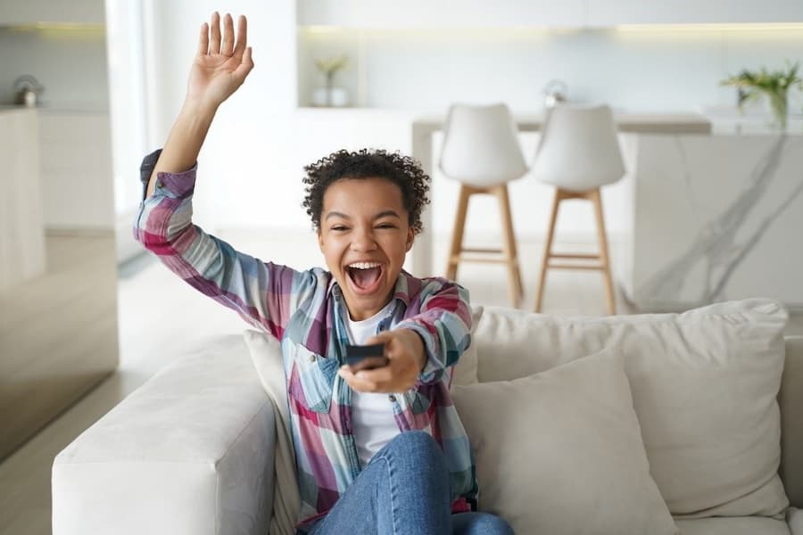 A young person holding a remote control and raising her hand